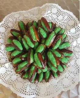 Dattes farcies à la pâte d'amande verte, posées sur une dentelle de papier.