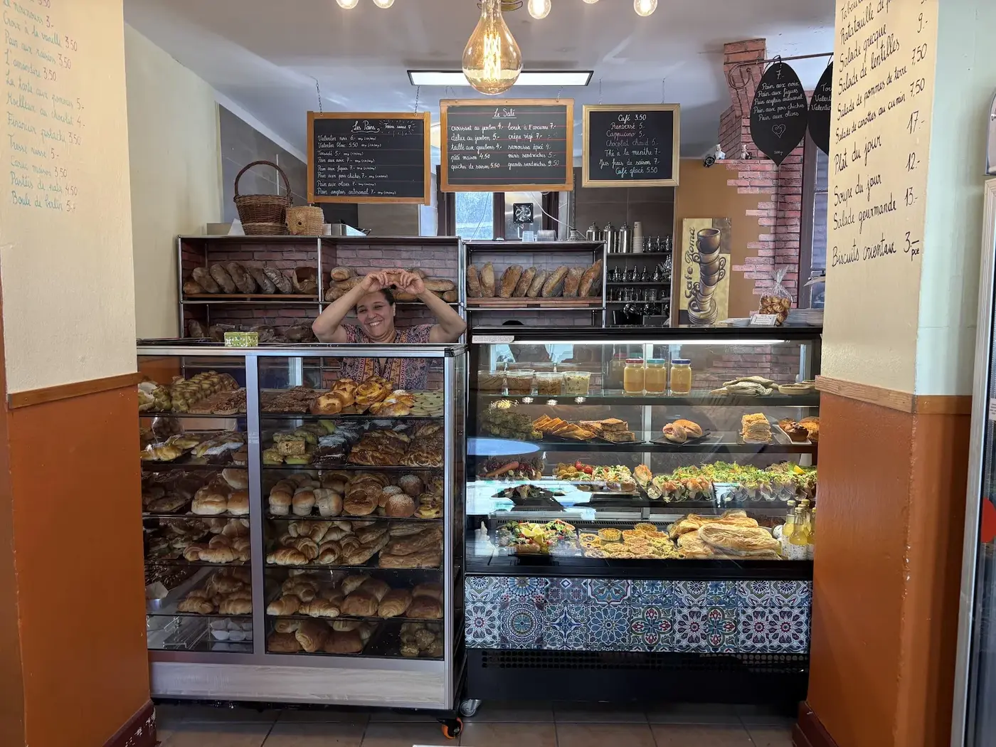 Farah derrière son comptoir, entre les étagères de pain à gauche et les vitrines de pâtisseries à droite.