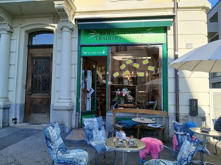 Devanture verte de la boulangerie : enseigne « Boulangerie Traditionnelle », porte ouverte, terrasse avec chaises en fer.