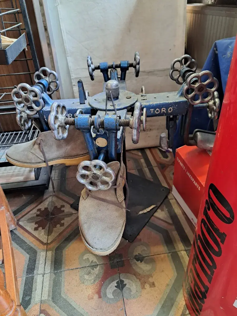 Machine à coudre vintage TORO devant des bottes en suède en cours de réparation, sol carrelage motif géométrique.