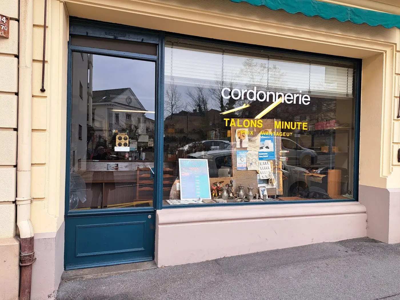 Devanture de la Cordonnerie du Reposoir : façade crème, encadrement vitrine bleu sarcelle, lettrage jaune cordonnerie et talons minute prix avantageux.