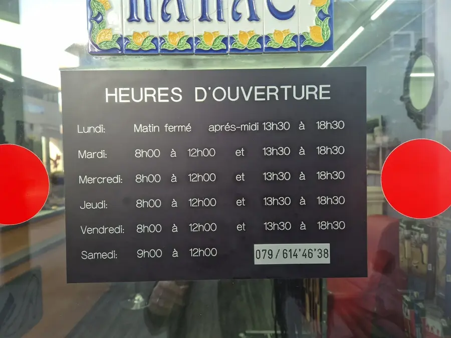 Panneau heures d'ouverture noir et blanc accroché à la vitrine, avec au-dessus la frise de faïence portugaise jaune, vert et bleu cobalt.