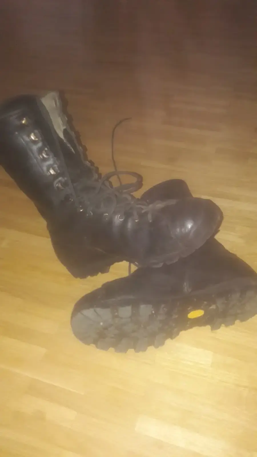 Paire de bottes en cuir noir avec lacets, semelles Vibram visibles avec leur logo jaune, en cours de réparation dans l'atelier.